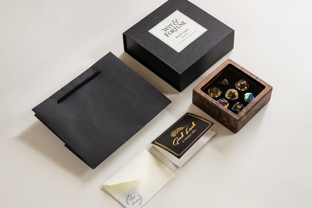 Black gift box, bag, greeting card and wooden case displaying rainbow-reflective glass dice.