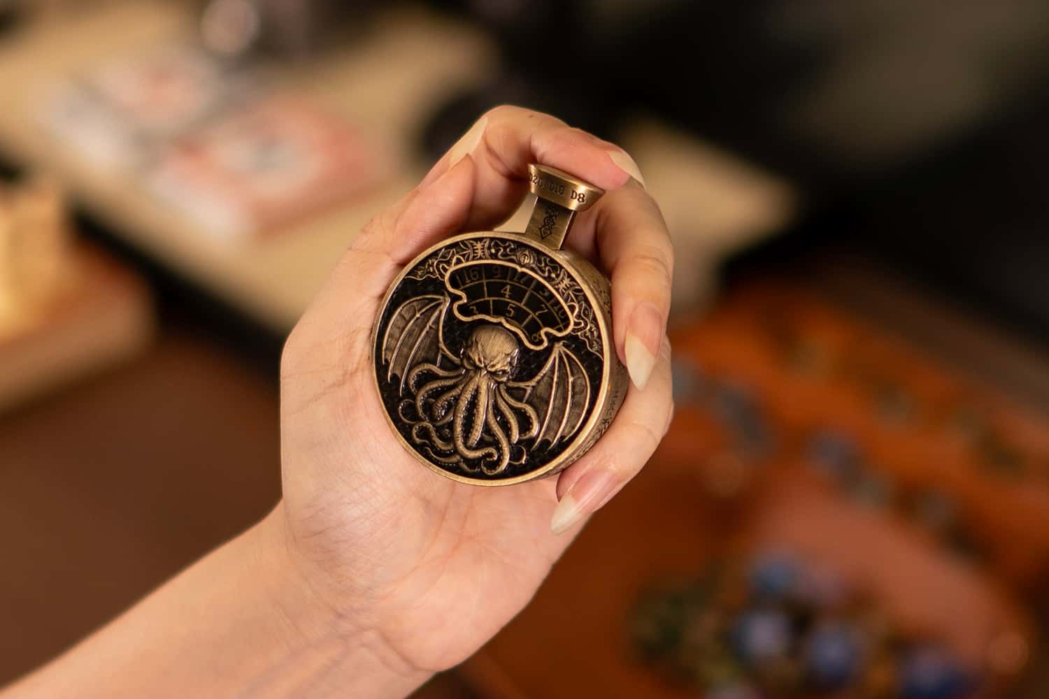Hand holding an antique bronze Pocket Press Dice with raised dragon detailing.