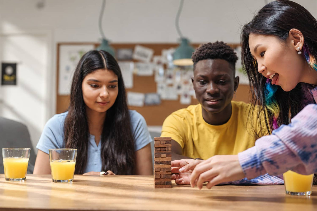 Three friends playing a wooden block-stacking game at a table