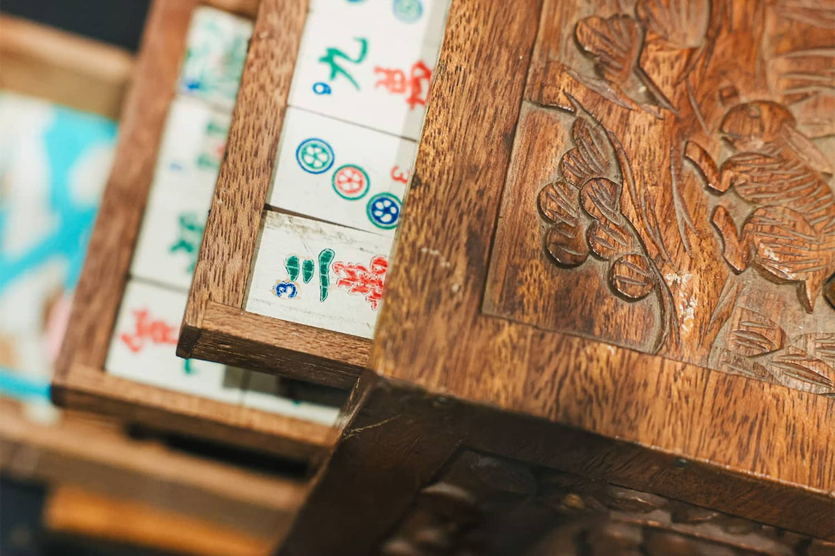 Traditional mahjong tiles arranged inside a carved wooden storage box.