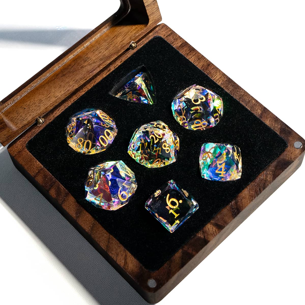 Seven rainbow-reflective glass dice with gold numbers in an open wooden case.