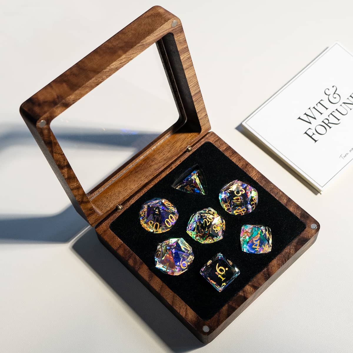 Open wooden dice case with seven rainbow-reflective dice and a Wit & Fortune card.
