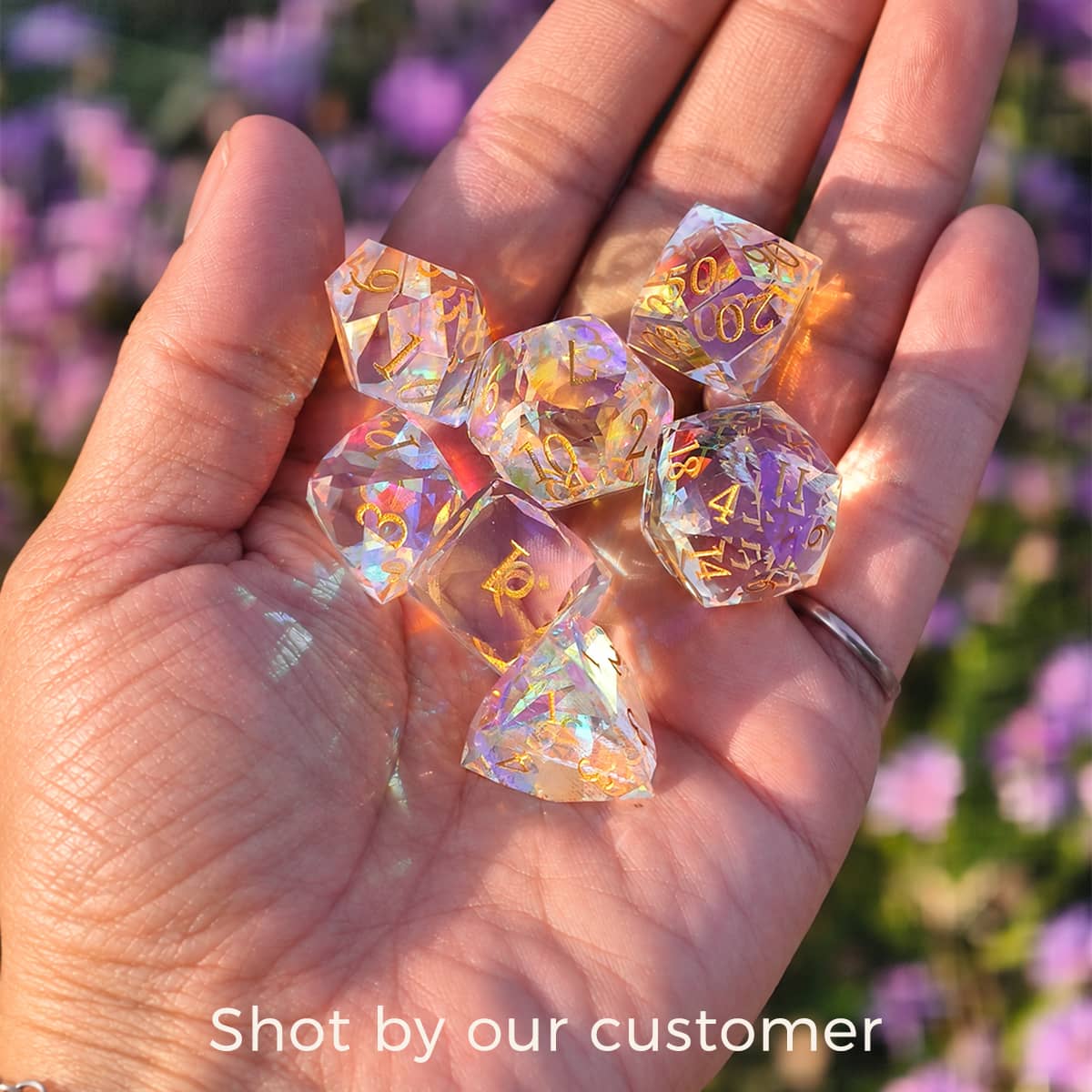 Customer photo of a hand holding a rainbow-reflective glass dice set in sunlight.