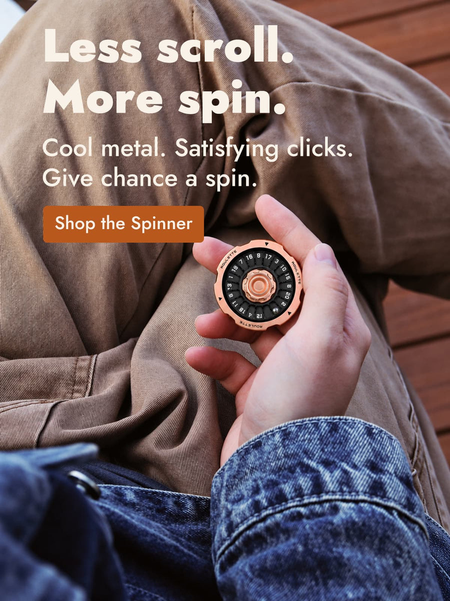 Eine Hand hält einen schwarz-roségoldfarbenen D20-Spinner über einer braunen Hose.