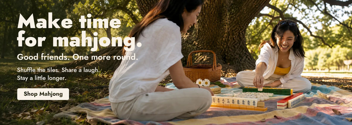 Zwei Freunde spielen Mahjong auf einer Picknickdecke unter einem Baum.