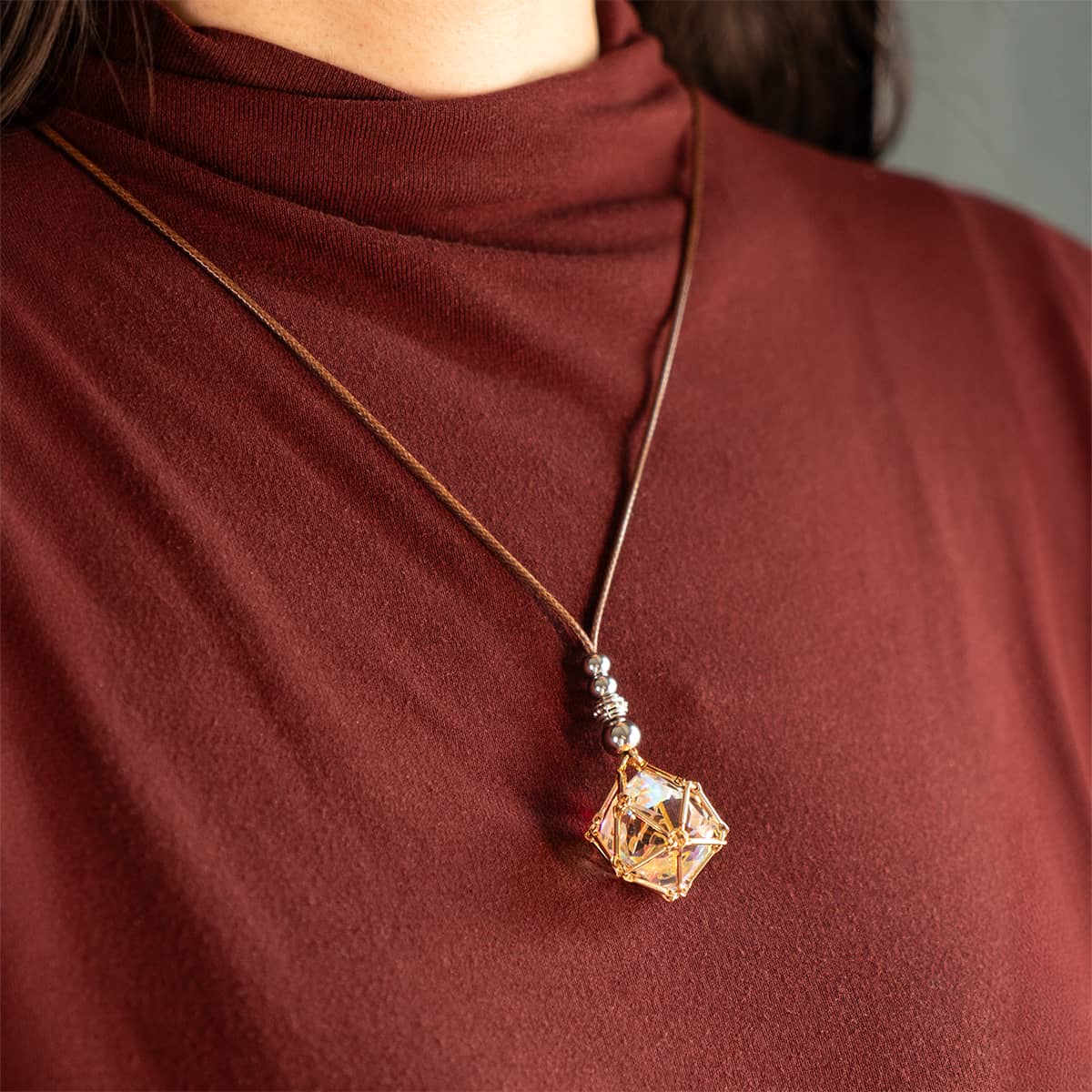 Person wearing a rainbow-reflective die pendant on a brown cord necklace.